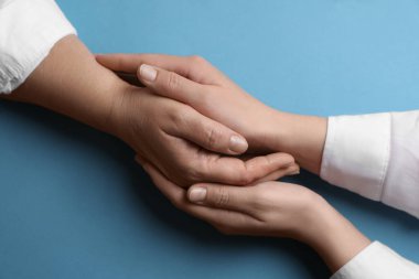 Açık mavi arka planda annesiyle el ele tutuşan bir kadın.