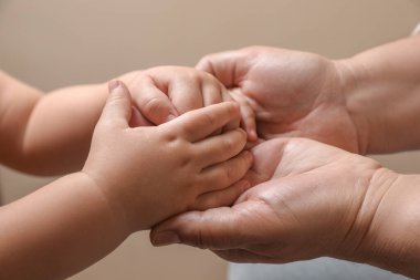 Bej arka planda torunuyla el ele tutuşan kadın, yakın plan.