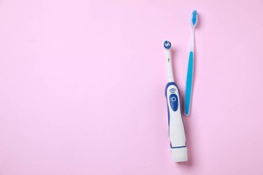 Pembe arka planda elektrikli ve plastik diş fırçaları. Metin için boşluk