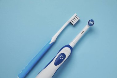 Turkuaz arka planda elektrikli ve plastik diş fırçaları, düz konum