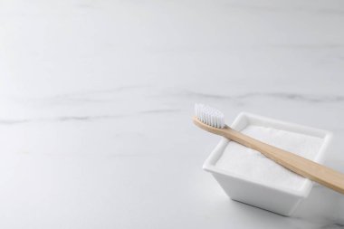 Bambu diş fırçası ve bir kase kabartma tozu beyaz masada, yakın plan. Metin için boşluk