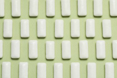 Açık yeşil arka planda dişeti çiğneyen lezzetli beyaz sakızlar.