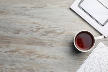 Beyaz ahşap masada seramik bardak aromatik çay, klavye, kitap ve akıllı telefon, düz yatak. Metin için boşluk