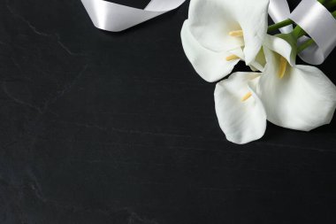 Güzel zambak çiçekleri ve siyah masanın üstünde beyaz kurdele, üzerinde yazı için yer var. Cenaze sembolleri
