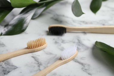 Bambu diş fırçaları ve yeşil yapraklar beyaz mermer masada, yakın plan.
