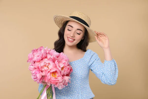 美しいです若いです女性でわら帽子でピンク牡丹の花束とともにベージュの背景 — ストック写真