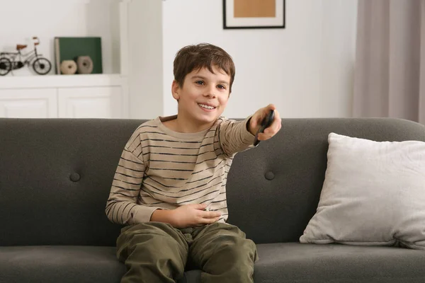 Happy boy changing TV channels with remote control on sofa at home