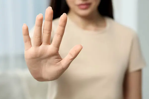 Woman showing stop gesture indoors, selective focus