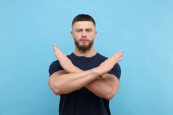 Stop gesture. Man with crossed hands on light blue background