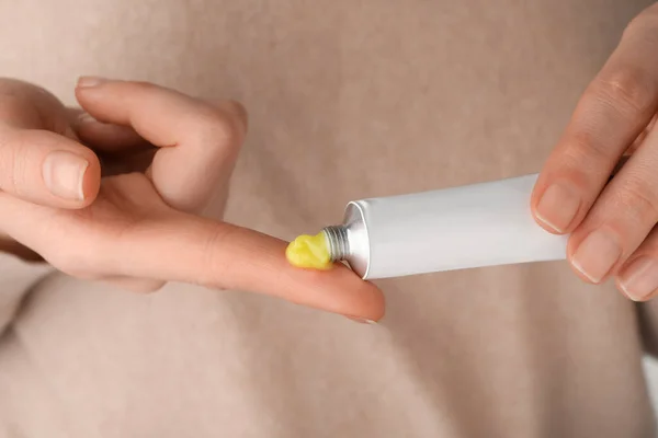 Woman squeezing out ointment from tube on her finger, closeup