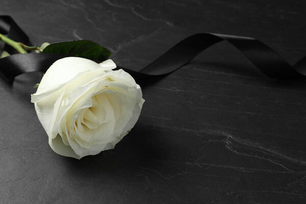 White rose and ribbon on black table, closeup with space for text. Funeral symbols