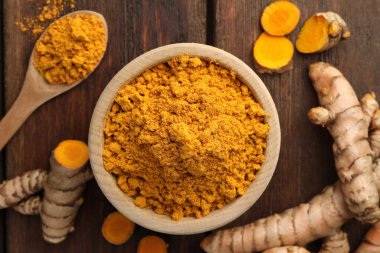 Aromatik zerdeçal tozu ve ahşap masa üzerinde çiğ kökler.