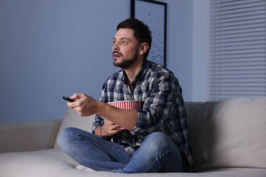 Patlamış mısır kovalı bir adam akşam evde uzaktan kumandayla televizyon kanallarını değiştiriyor.