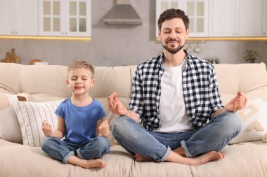 Baba oğul evdeki kanepede birlikte meditasyon yapıyorlar. Ahenk ve zen