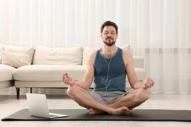 Spor kıyafetli bir adam evde dizüstü bilgisayarın yanında meditasyon yapıyor. Ahenk ve zen
