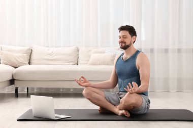 Spor kıyafetli bir adam evde dizüstü bilgisayarın yanında meditasyon yapıyor. Ahenk ve zen