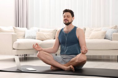 Spor kıyafetli bir adam evde dizüstü bilgisayarın yanında meditasyon yapıyor. Ahenk ve zen