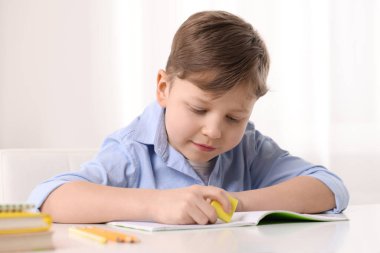 Küçük çocuk içerideki beyaz masadaki defterindeki hatayı siliyor.