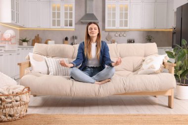 Evdeki kanepede meditasyon yapan bir kadın. Ahenk ve zen