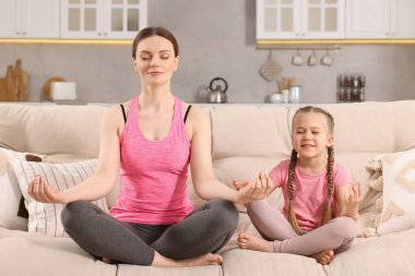 Anne ve kızı evdeki kanepede meditasyon yapıyorlar. Ahenk ve zen