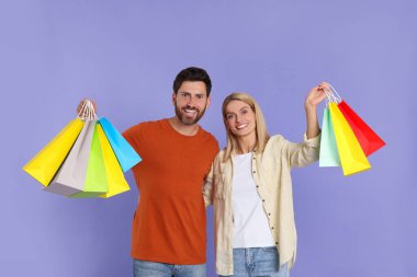 Aile alışverişi. Menekşe arka planda renkli çantaları olan mutlu çift.