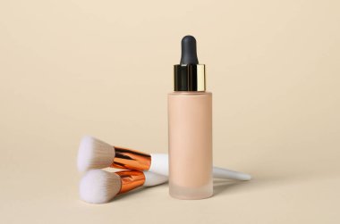 Bir şişe deri temeli ve bej arka planda fırçalar. Makyaj ürünü