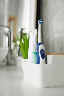 Banyodaki beyaz tezgahta elektrikli diş fırçaları ve bir tüp macun.