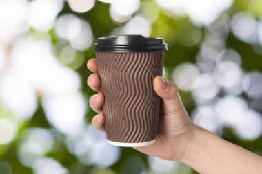 İçmek için. Bulanık yeşil arka planda elinde kahve bardağı tutan kadın, yakın plan.