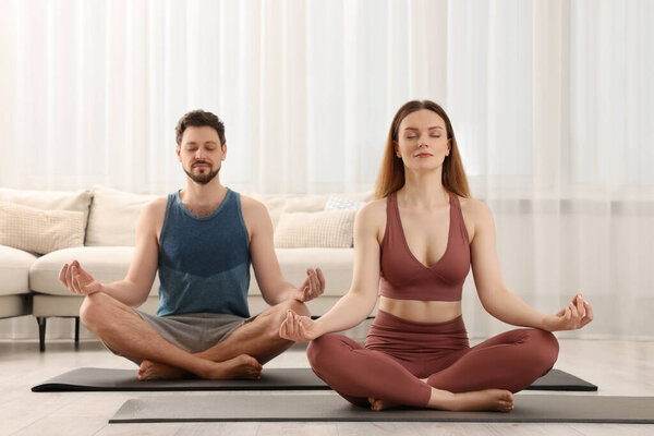 Couple in sportswear meditating together at home. Harmony and zen