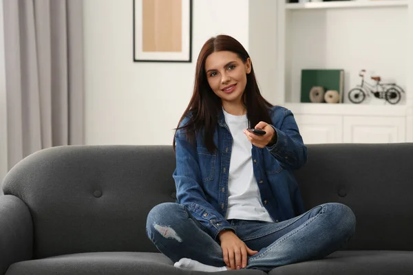 Happy woman changing TV channels with remote control on sofa at home