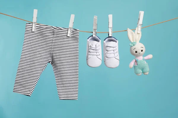 Çizgili bebek pantolonu, ayakkabısı ve örgü oyuncağı turkuaz arka planda çamaşır ipinde kuruyor.