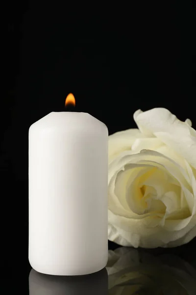 stock image White rose and burning candle on black mirror surface in darkness, closeup. Funeral symbols