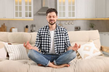 Evdeki kanepede meditasyon yapan bir adam. Ahenk ve zen