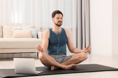 Spor kıyafetli bir adam evde dizüstü bilgisayarın yanında meditasyon yapıyor. Ahenk ve zen