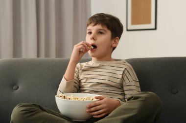 Küçük çocuk evde televizyon izlerken patlamış mısır yiyor.