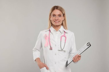 Pembe kurdeleli doktor, dosya ve açık gri arka planda steteskop. Göğüs kanseri farkındalığı