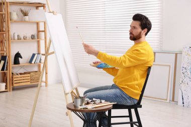 Stüdyoda resim yapan adam. Tuvali tutmak için resim sehpası kullanılıyor