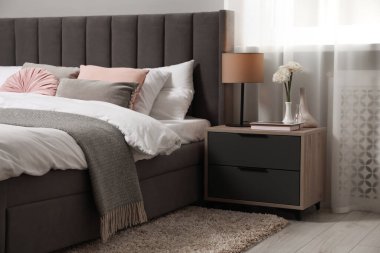 Yatak, yastıklar, lamba ve odadaki komodinin üzerinde farklı dekorlar. Şık iç mekan