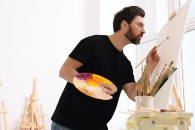 Stüdyoda resim yapan adam. Tuvali tutmak için resim sehpası kullanılıyor