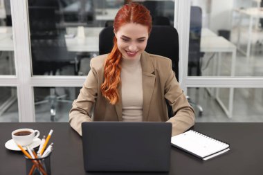Ofisteki siyah masada bilgisayarla çalışan mutlu kadın.