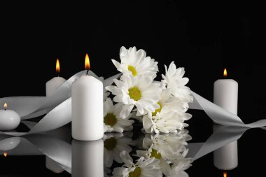Beyaz kasımpatı çiçekleri ve siyah ayna yüzeyinde yanan mumlar karanlıkta. Cenaze sembolleri