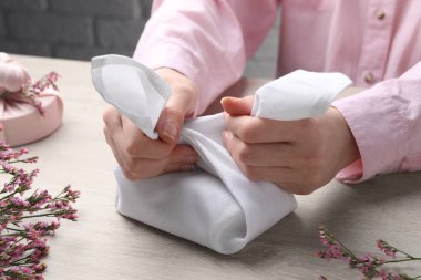 Furoshiki tekniği. Kadın hediyesini beyaz kumaşla kaplıyor, ahşap masada, yakın plan.