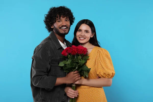 International dating. Happy couple with bouquet of roses on light blue background