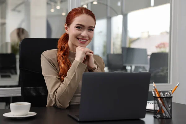 一个快乐的女人在办公室的黑桌边和笔记本电脑一起工作 — 图库照片