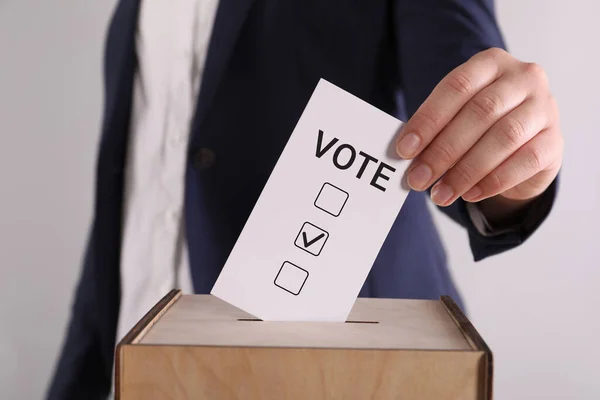 ライトグレーの背景に投票ボックスに紙を置く女性 — ストック写真