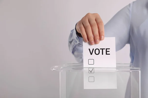 ライトグレーの背景に投票ボックスに紙を置く女性 — ストック写真