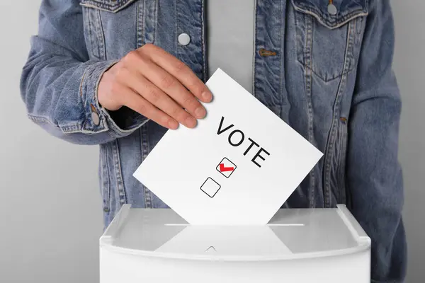 ライトグレーの背景に紙を投票して投票箱に入れる男 — ストック写真