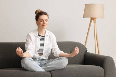 Evdeki kanepede meditasyon yapan bir kadın. Ahenk ve zen