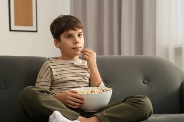 Küçük çocuk evde televizyon izlerken patlamış mısır yiyor.