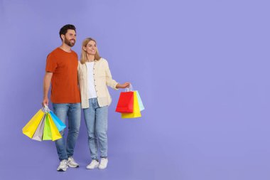 Aile alışverişi. Menekşe arkaplanda renkli çantaları olan mutlu bir çift. Metin için boşluk